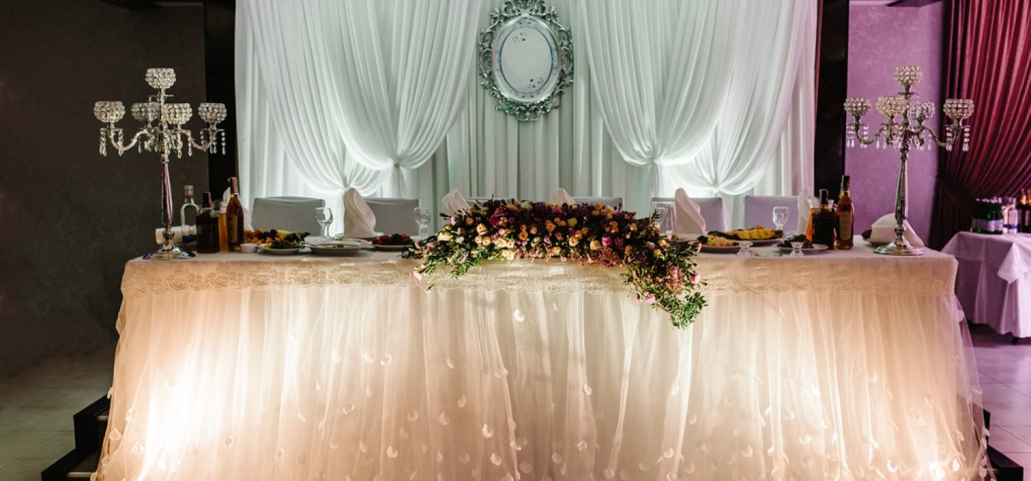 Festive table decorated with composition of pink flowers and greenery in the banquet hall. Table newlyweds in the banquet area on wedding party.
